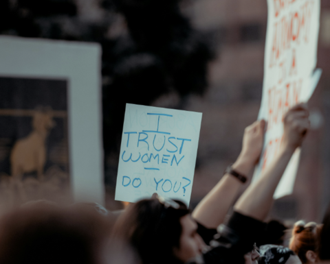 Protesters with signs, focus on a poster saying "I trust women - Do you?"