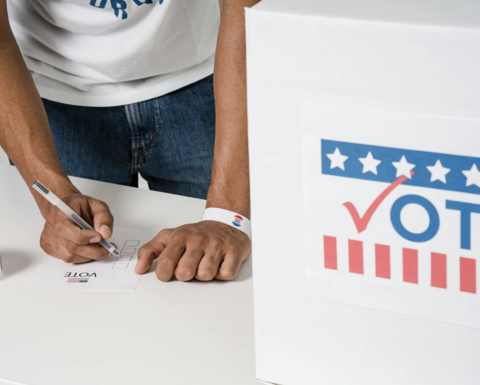 Man filling out a voter registration form, next to a voting box that says "vote"